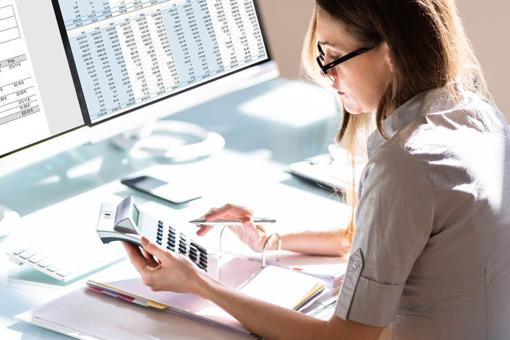 A woman holding a calculator while working at her desk. Here are 11 quick job certifications that pay well.