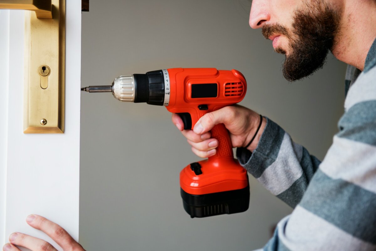 man fixing a door handle with a cordless drill in his hand