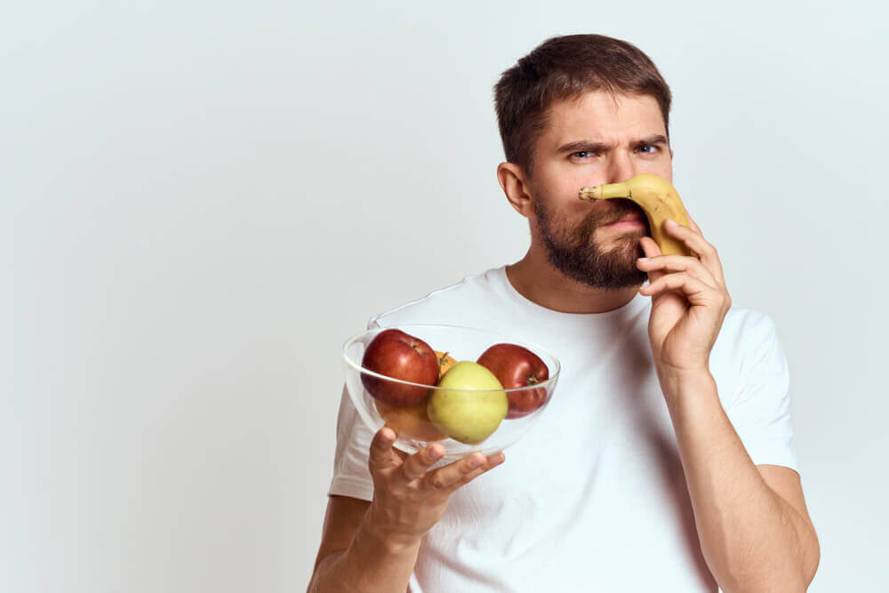 Man smelling fruit with disgusted look on his face