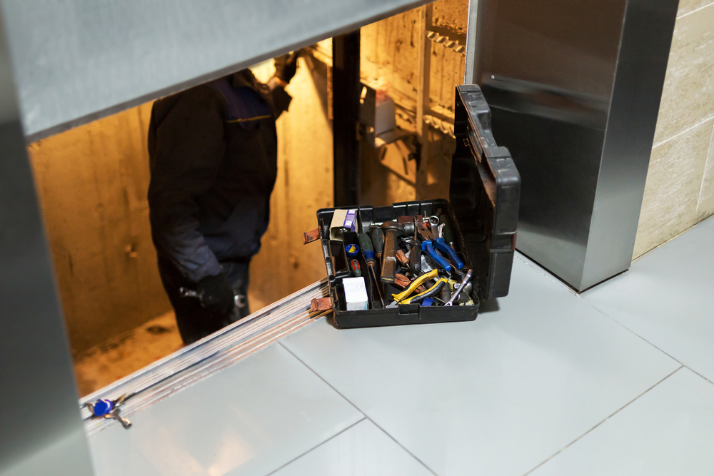 Technician working inside an open elevator shaft beside a toolbox