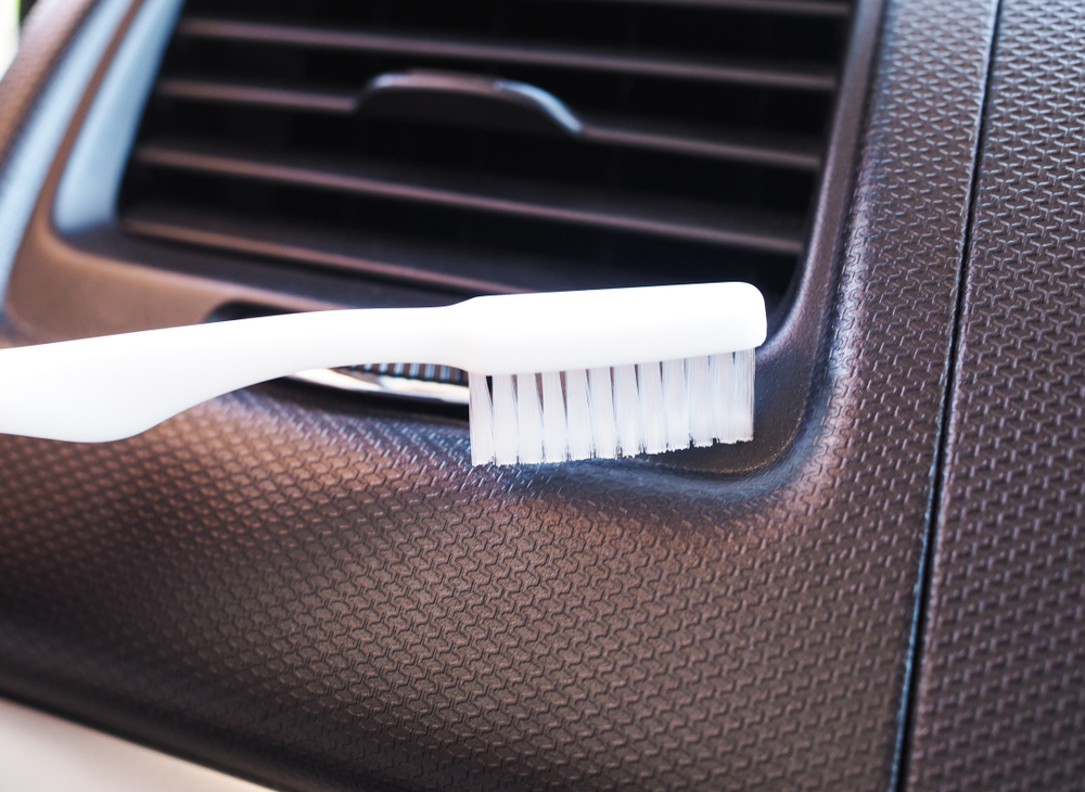 Small brush cleaning dust from a car dashboard air vent