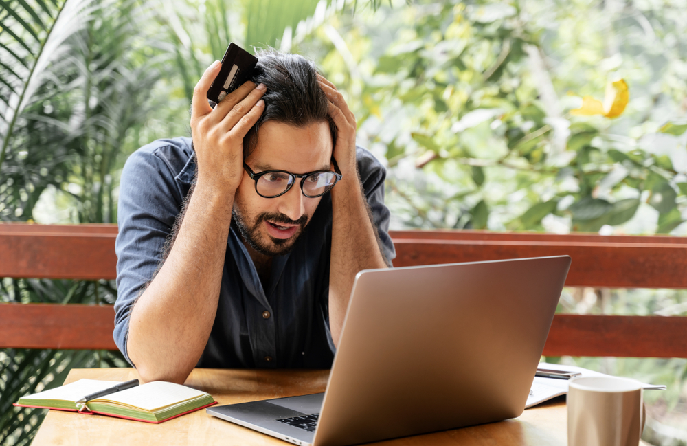 Worried man holding a bank card while looking at a laptop