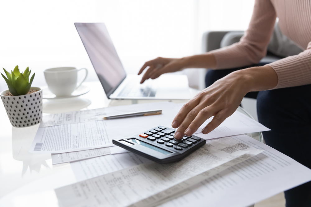 Woman reviewing paperwork with a calculator beside her laptop