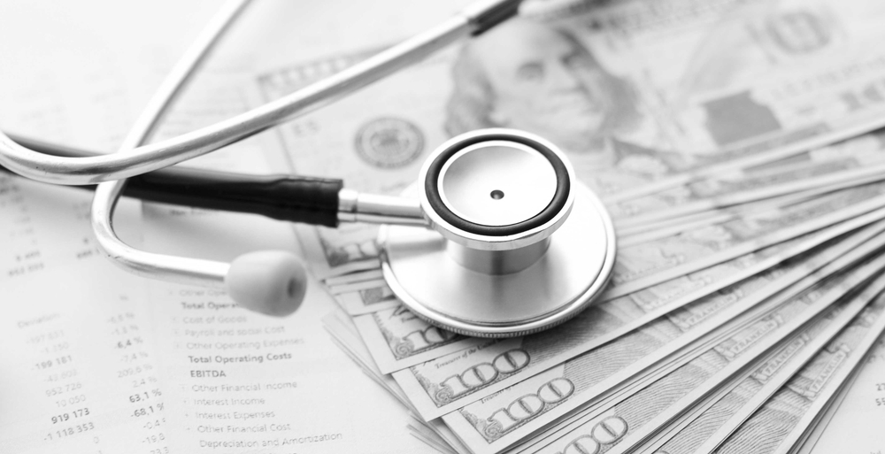 Stethoscope resting on U.S. currency and financial paperwork