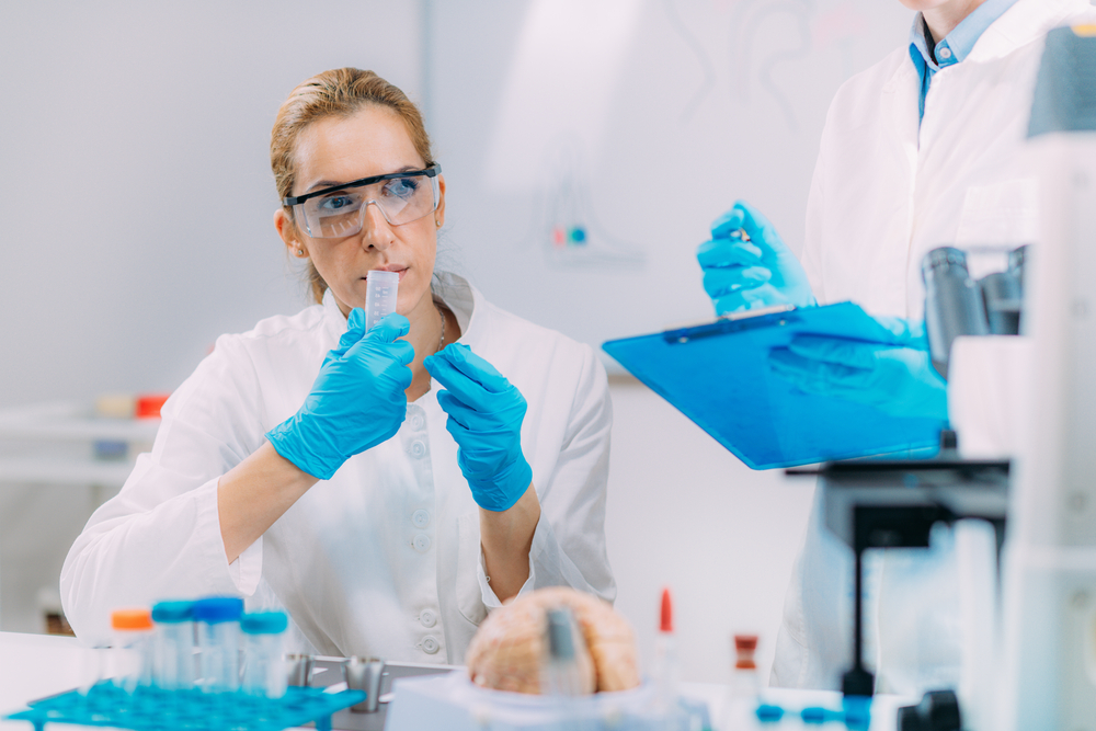 Laboratory scientist smelling a sample while a colleague records the results