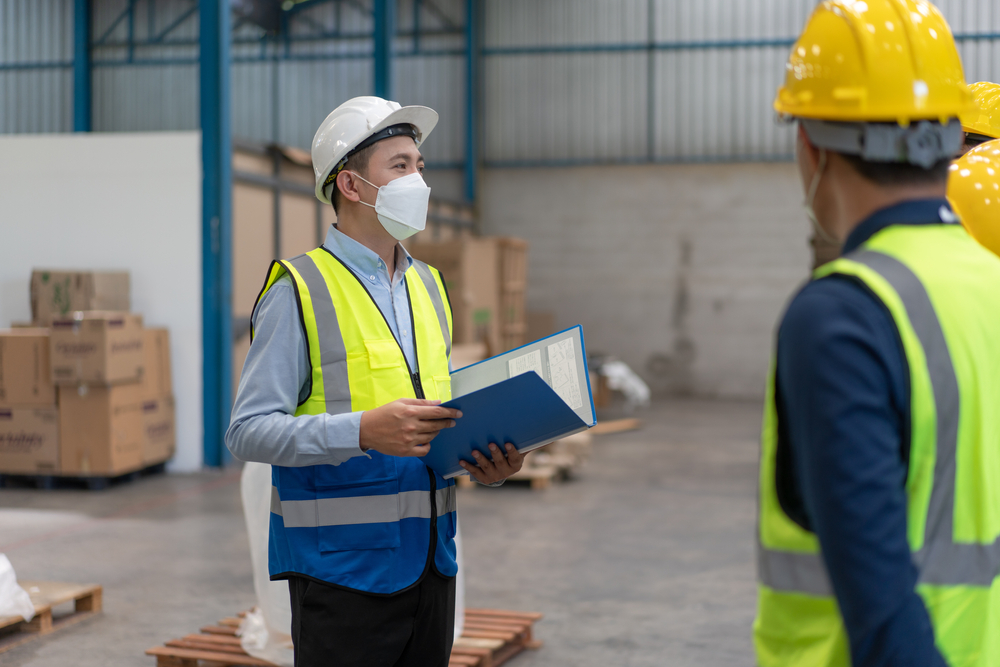 Safety professional in a hard hat reviewing documents with warehouse workers