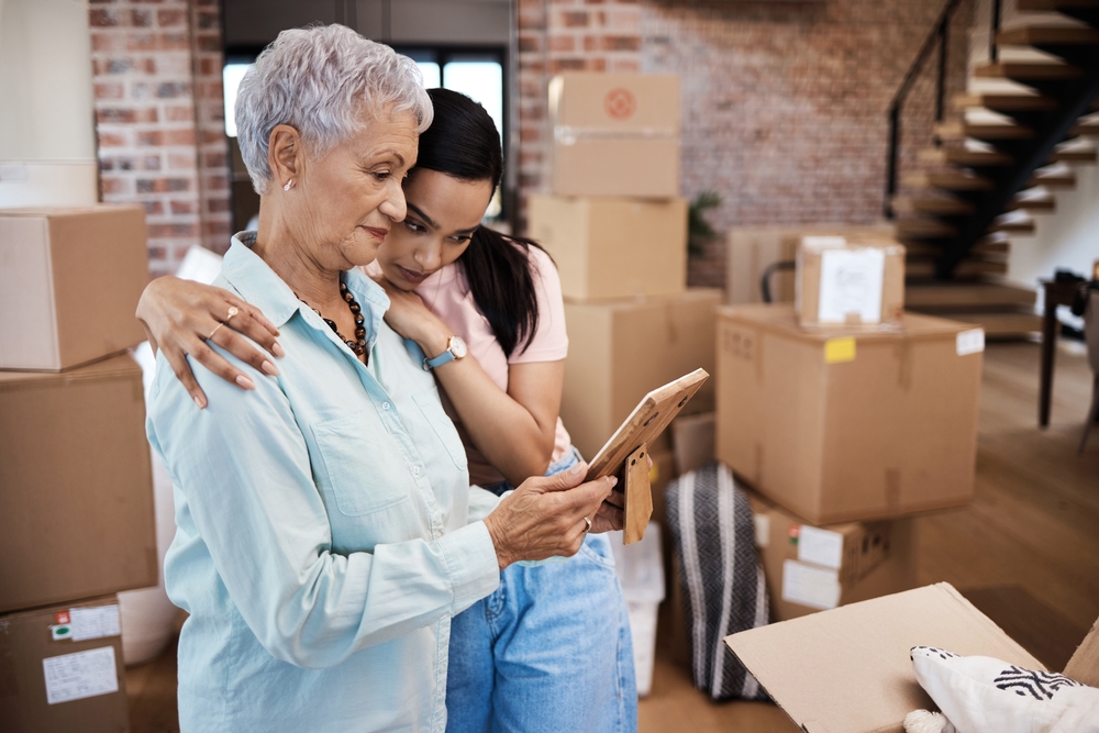 Older woman and younger woman reviewing a framed photograph among packed moving boxes