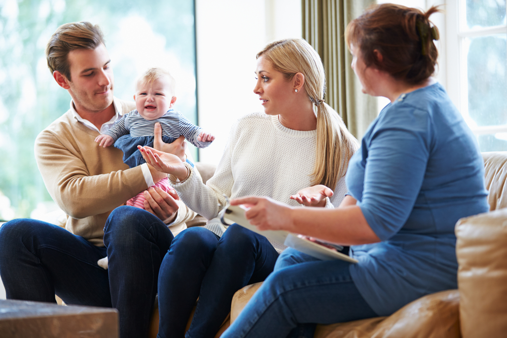 Social worker with a clipboard talking with parents and their baby at home