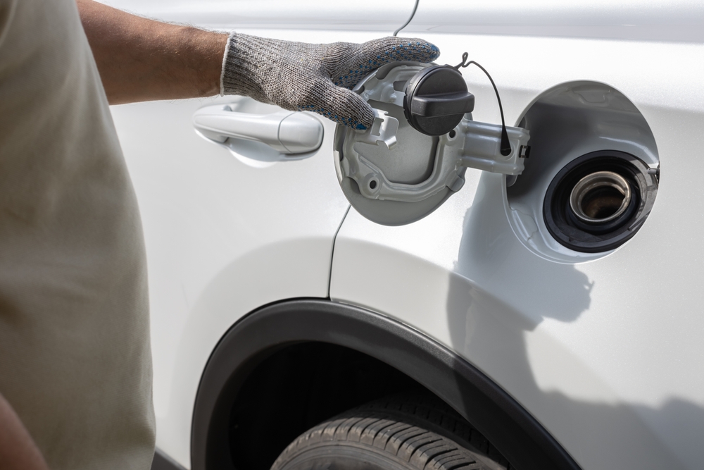 Gloved hand opening the fuel filler door of a white car