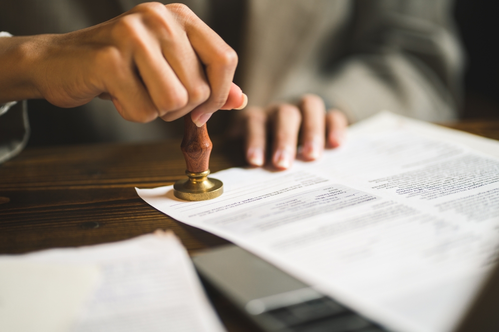 Hands pressing a wooden-handled stamp onto a legal document on a desk