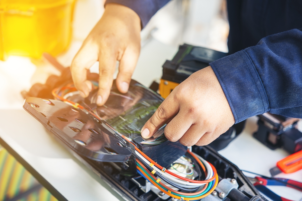 Hands arranging fiber optic strands in a splicing enclosure beside cable equipment