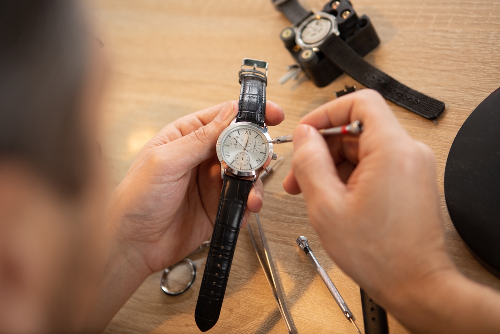 Watchmaker using a small tool to service a wristwatch at a workbench