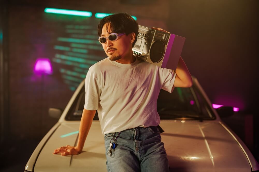 man listening to boom box leaning on his car