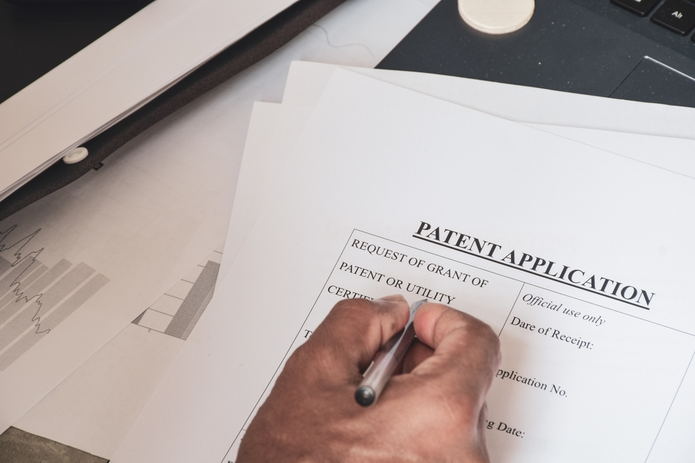 Hand completing a patent application form beside a laptop