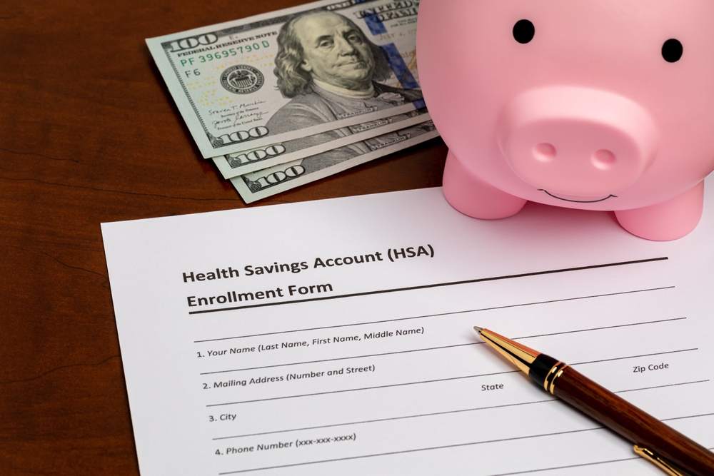 HSA enrollment form beside a pink piggy bank, dollar bills and a pen