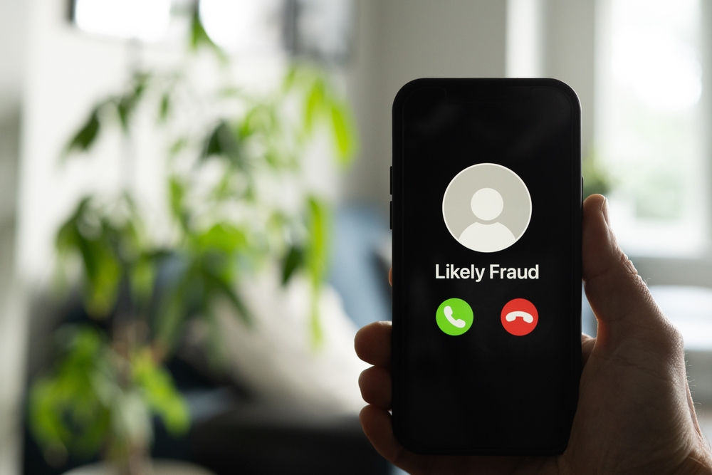Hand holding a smartphone with an incoming call labeled Likely Fraud