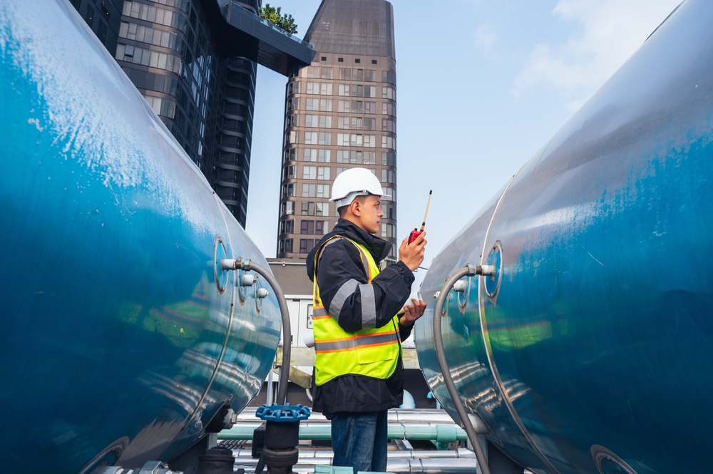 Worker wearing a hard hat and reflective vest between large blue industrial tanks