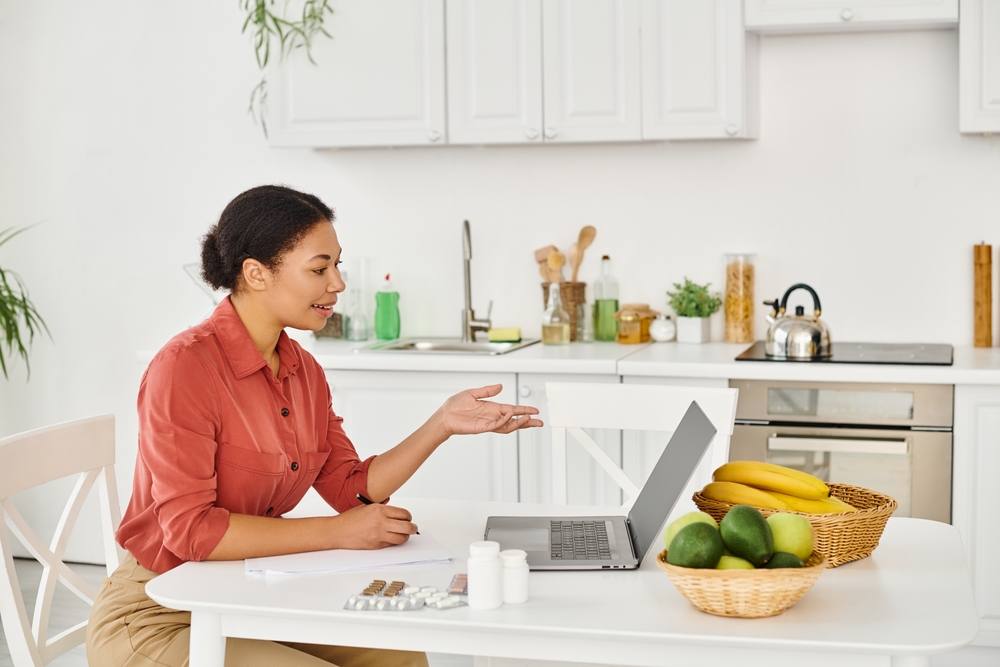 Dietitian taking notes during an online consultation beside fruit and a laptop
