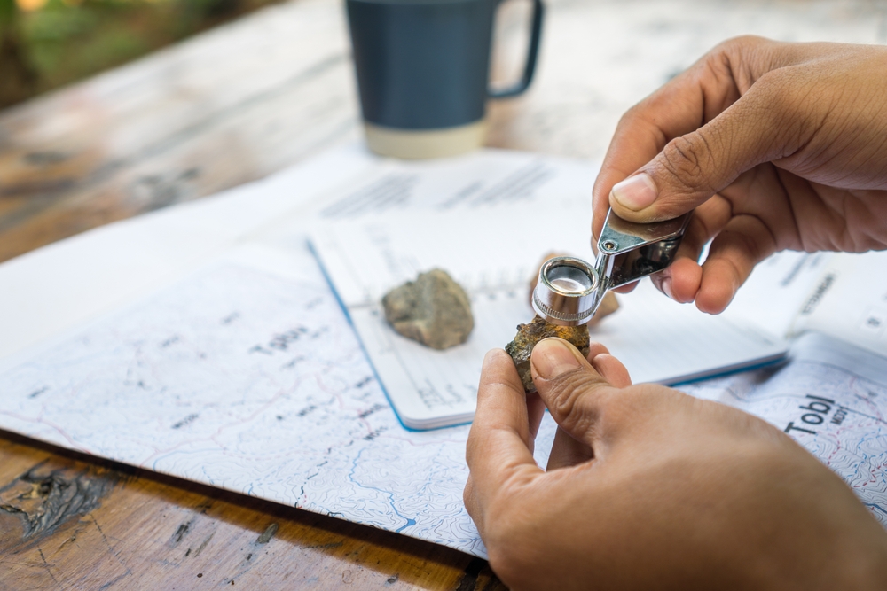 Geologist examining a rock sample with a hand lens over a field map and notebook
