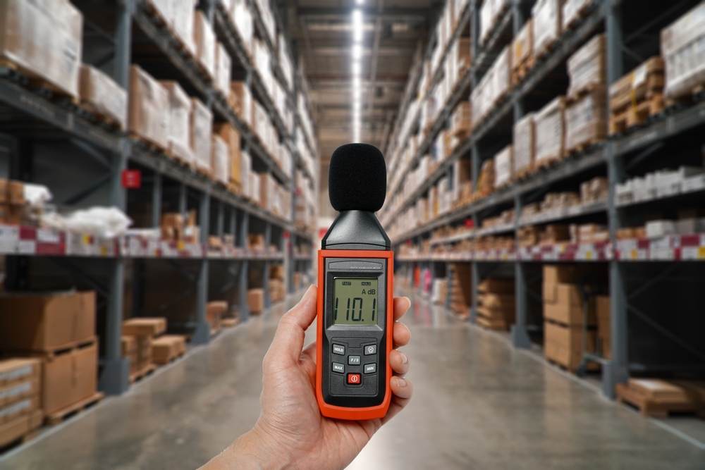 Hand holding a sound level meter to measure workplace noise in a warehouse