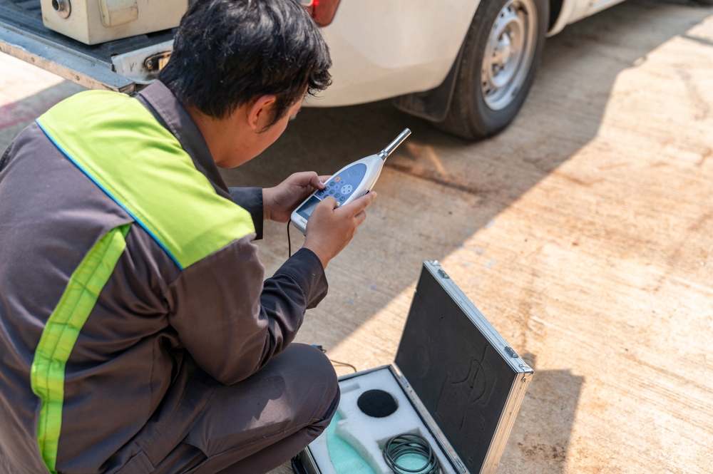 Worker setting up a handheld sound level meter beside an equipment case