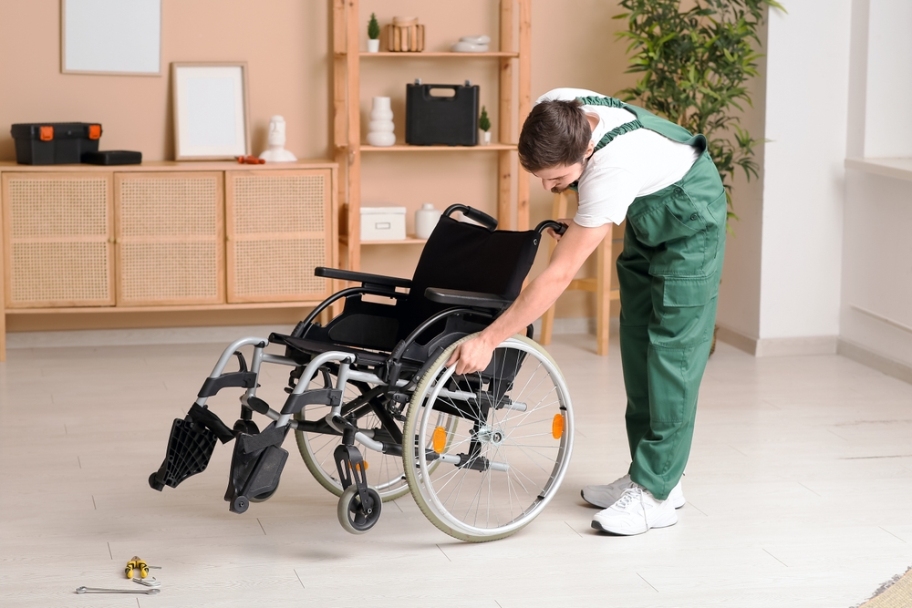 Technician checking the wheel and frame of a wheelchair beside repair tools