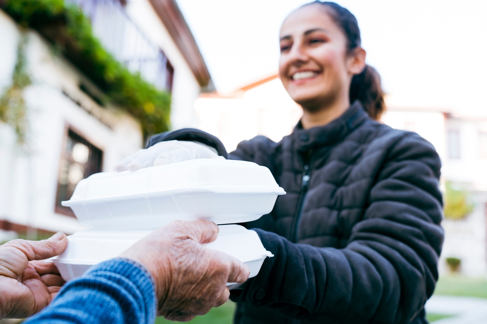 Volunteer handing prepared meal containers to an older person at home