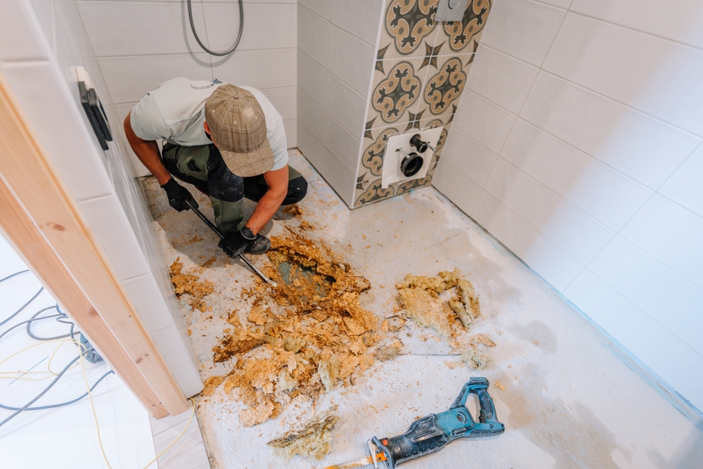 Worker removing damaged subfloor and insulation during a bathroom restoration