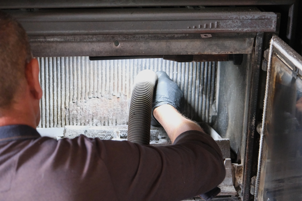 Chimney sweep using a vacuum hose to remove soot from the inside of a fireplace insert