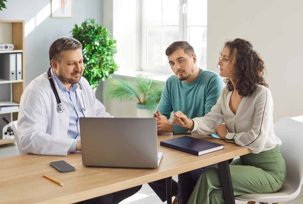Medical professional discussing information on a laptop with a couple in a clinic