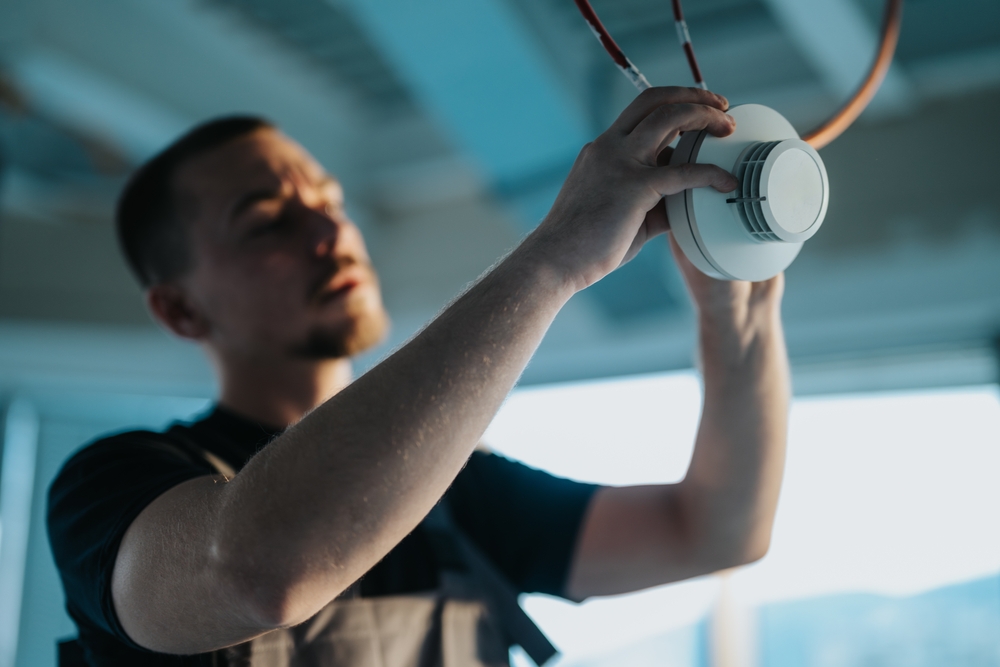 Technician fitting a smoke detector to a ceiling
