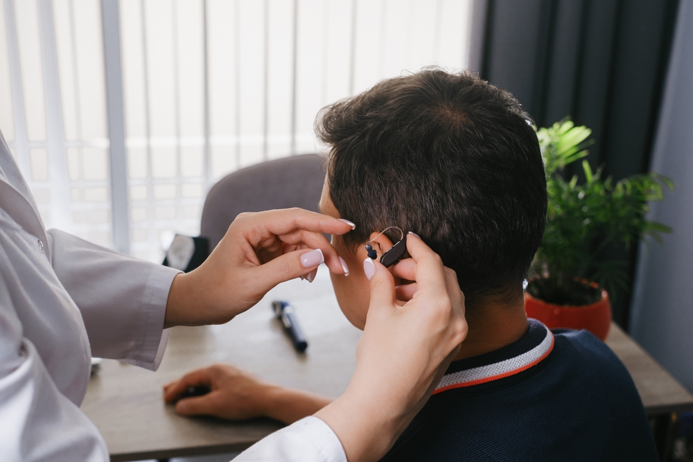 Clinician fitting a small behind-the-ear hearing aid on a patient