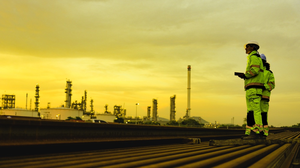 Engineers in protective clothing inspecting pipes at an industrial refinery