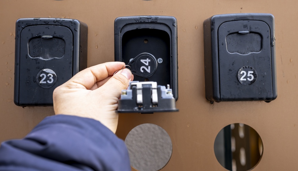 Hand retrieving an electronic key fob from an open wall-mounted rental lockbox