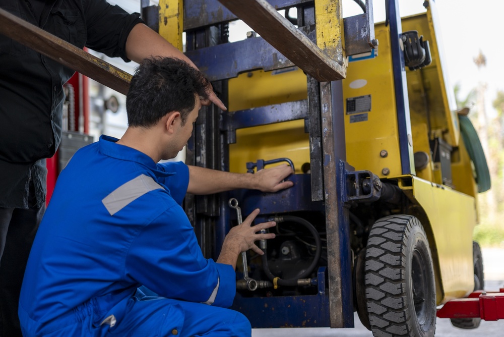 Forklift service technicians repairing forklift mast assembly Forklift service technicians inspecting and repairing the mast assembly of a yellow forklift