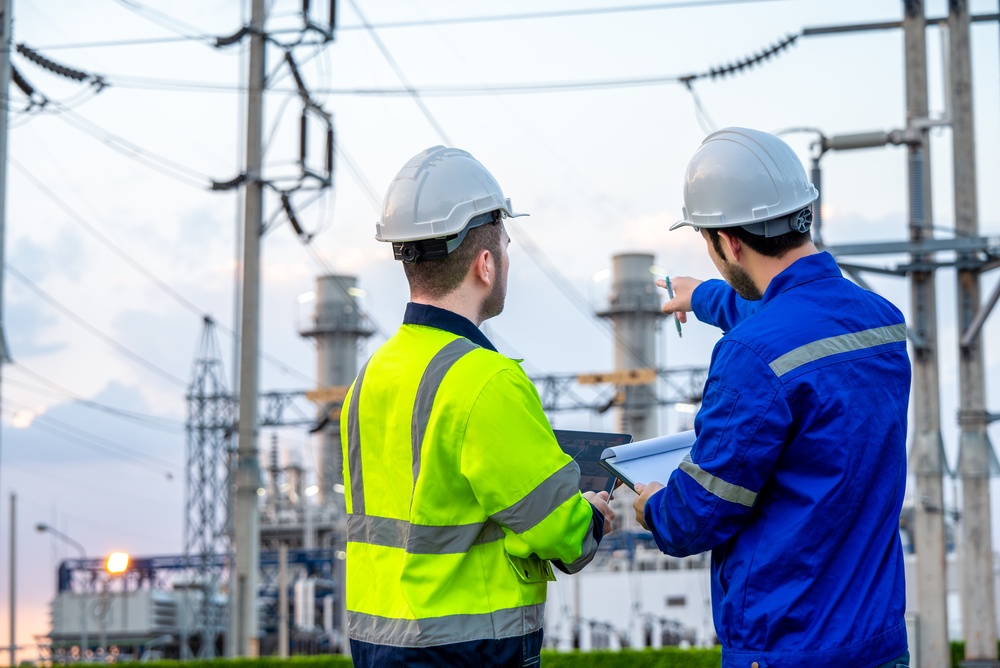 Two electrical professionals in hard hats reviewing plans and equipment at a substation