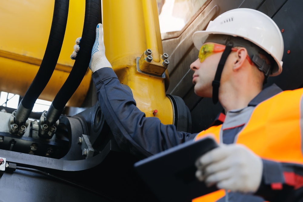 Hydraulic technician inspecting machinery hoses Hydraulic technician inspecting hydraulic hoses on construction machinery