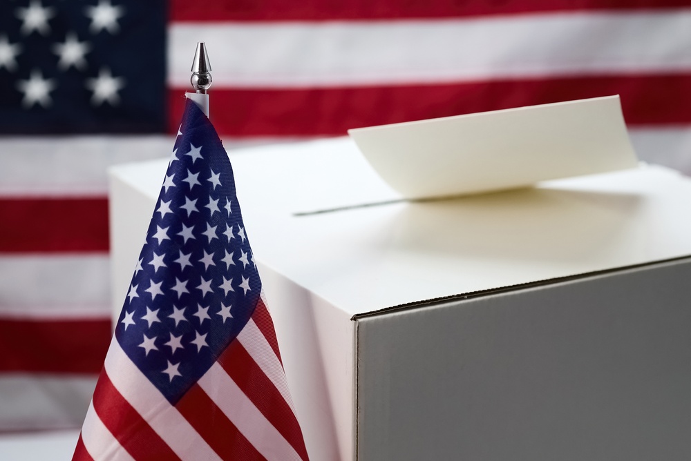 Ballot paper entering a white ballot box beside American flags