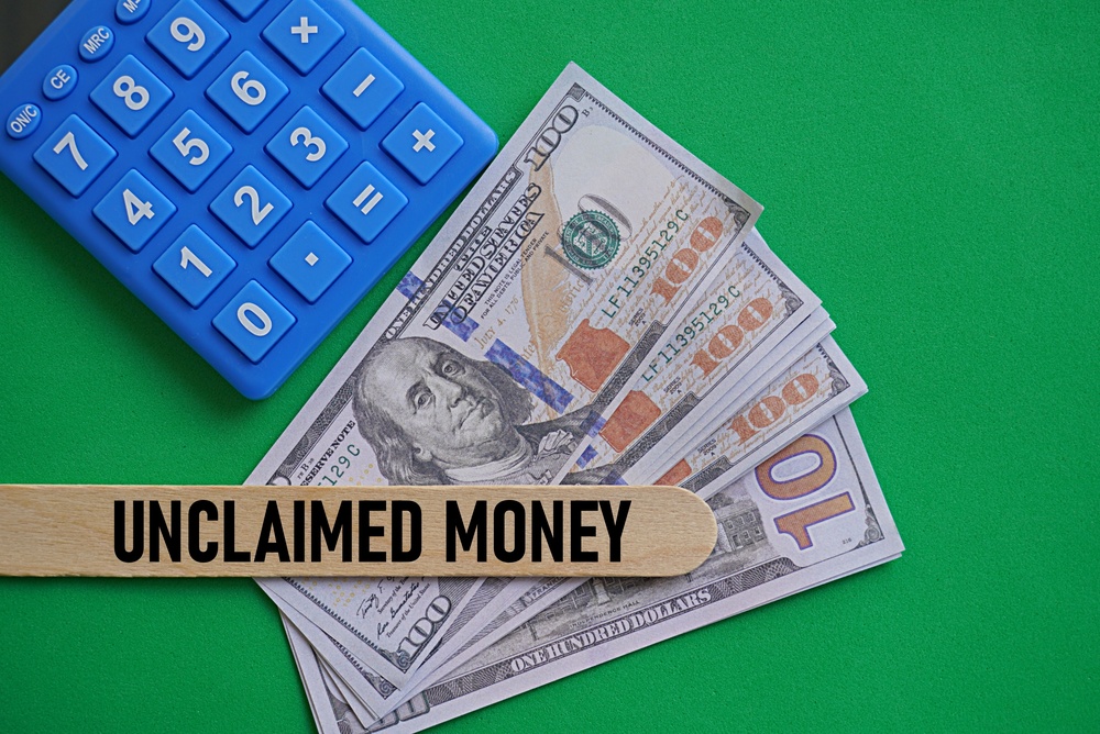 Unclaimed money label beside US dollar bills and a blue calculator