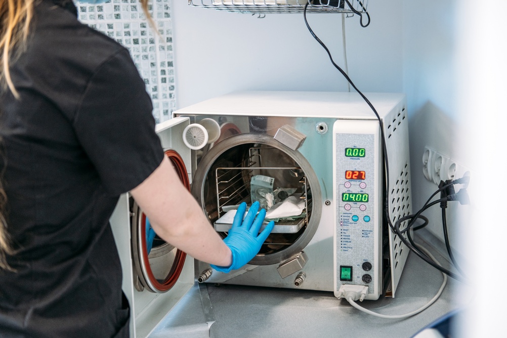 Gloved hand opening a medical autoclave containing instrument trays
