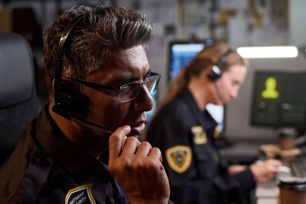 Uniformed dispatchers wearing headsets and monitoring screens in a public safety control room