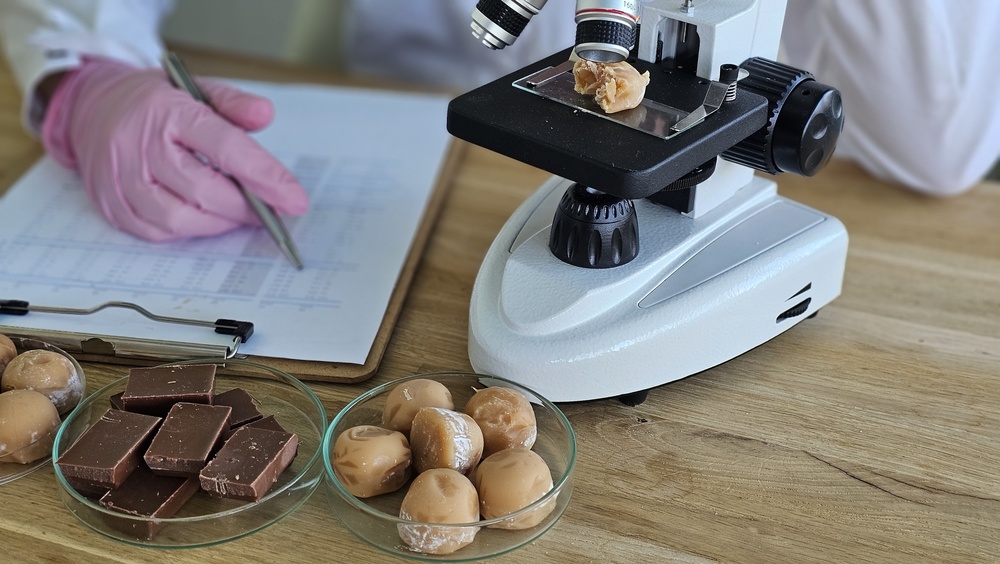 Food laboratory worker examining chocolate and candy samples beside a microscope and notes