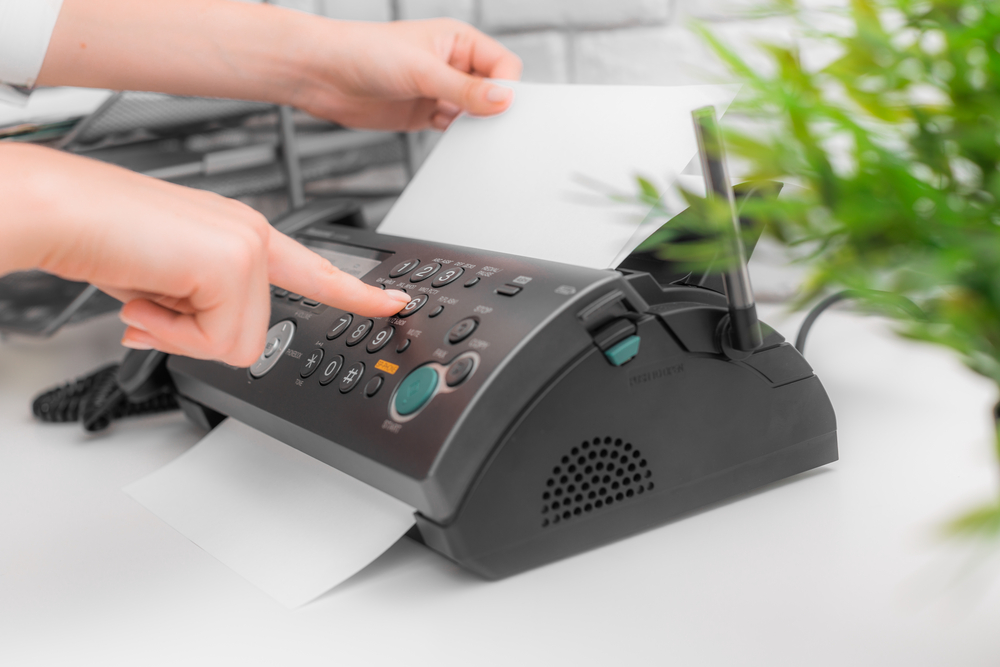 Hands feeding a document into an office fax machine and pressing its keypad