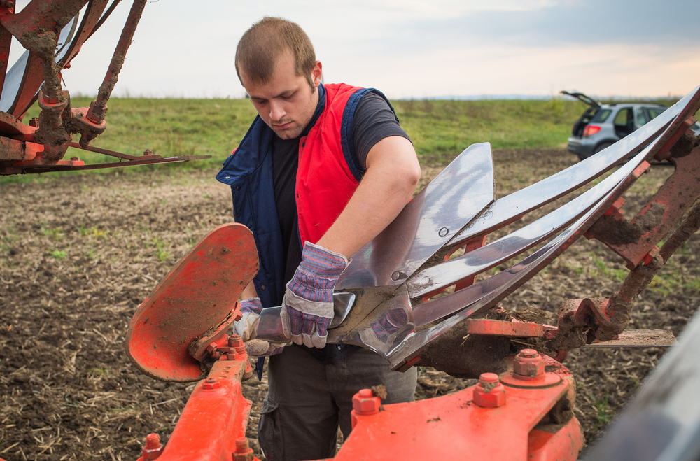 Agricultural equipment mechanic repairing tractor plow Agricultural equipment mechanic using tools to repair a plow attached to a tractor