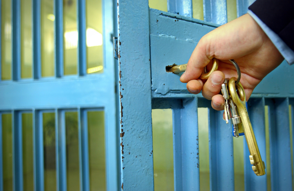 Hand holding a ring of keys while locking a barred prison door