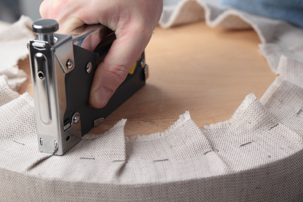 Upholsterer fastening fabric around a round stool seat with a staple gun