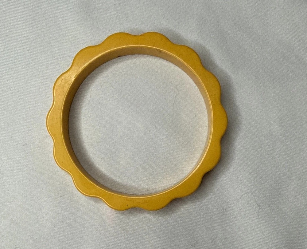 Butterscotch-yellow Bakelite bangle with a scalloped outer edge on pale fabric