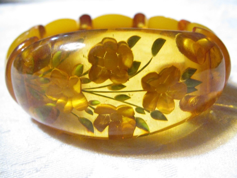 Translucent amber Bakelite bangle with reverse-carved flowers and green painted leaves
