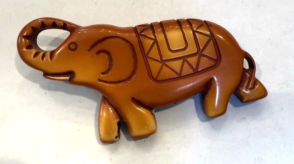 Warm brown Bakelite elephant brooch with raised trunk and a carved geometric saddle