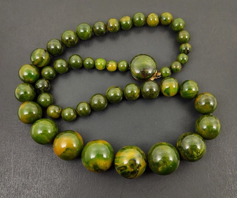 Graduated round Bakelite beads marbled in green and yellow, arranged on a dark background